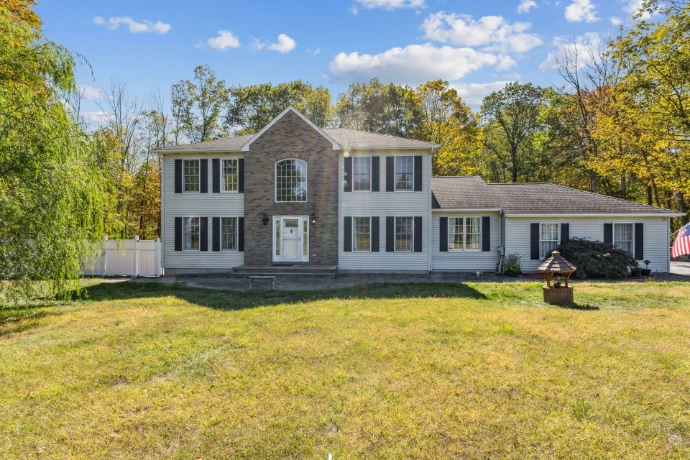Real estate photography in Passaic County, NJ, featuring a spacious colonial-style home with a stone entrance, large front lawn and wooded surroundings.
