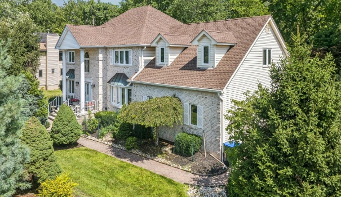 Real estate photography in Middlesex County, NJ, showing a spacious two-story home with light siding, landscaped gardens and mature trees.
